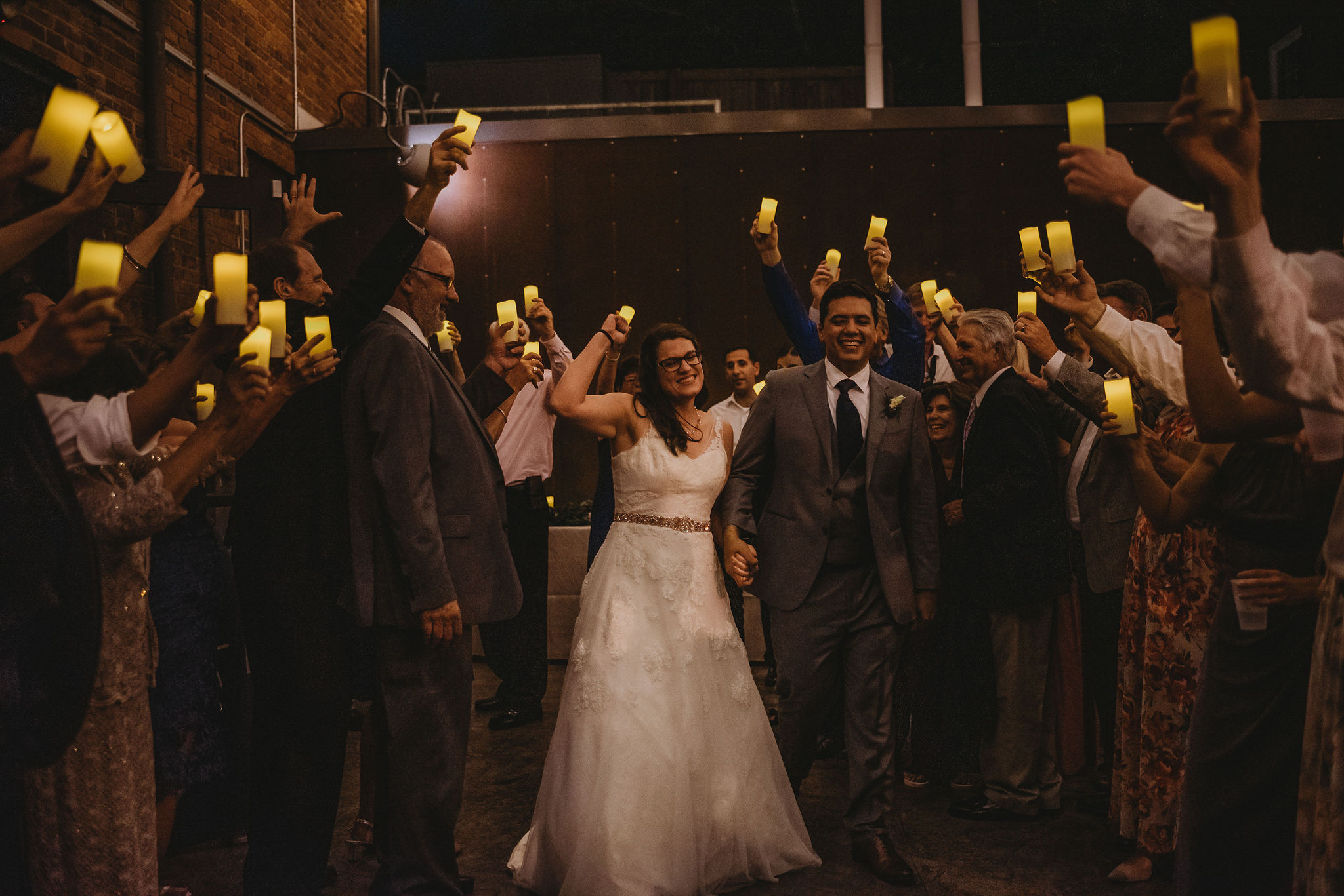 A bride & groom exit through a tunnel of their guests, who are holding LED candles. 