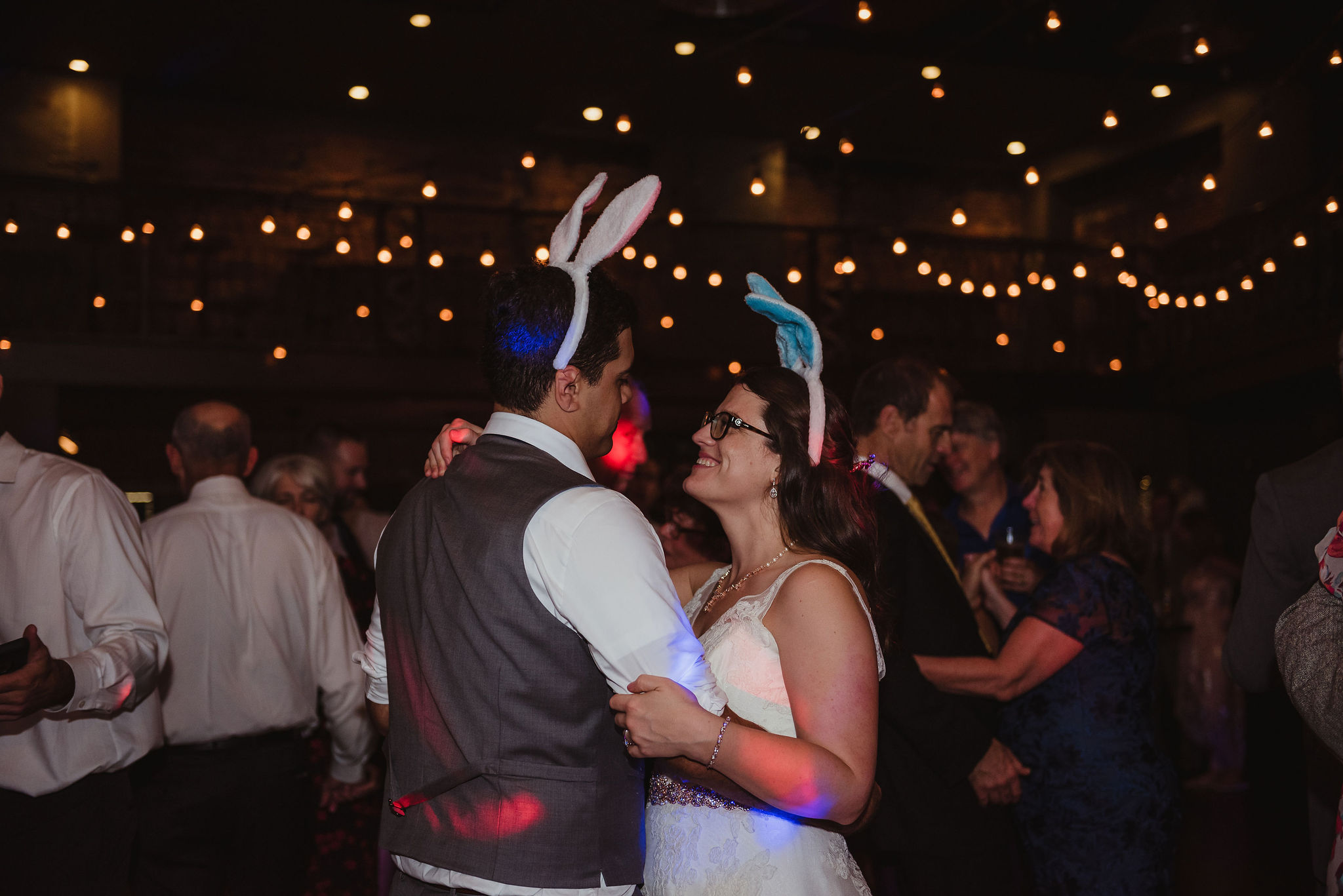 A groom and bride dance under market lights. They are wearing bunny ears.
