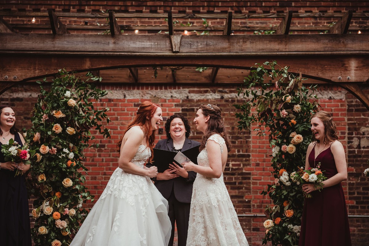 two brides and their officiant laugh during a wedding ceremony