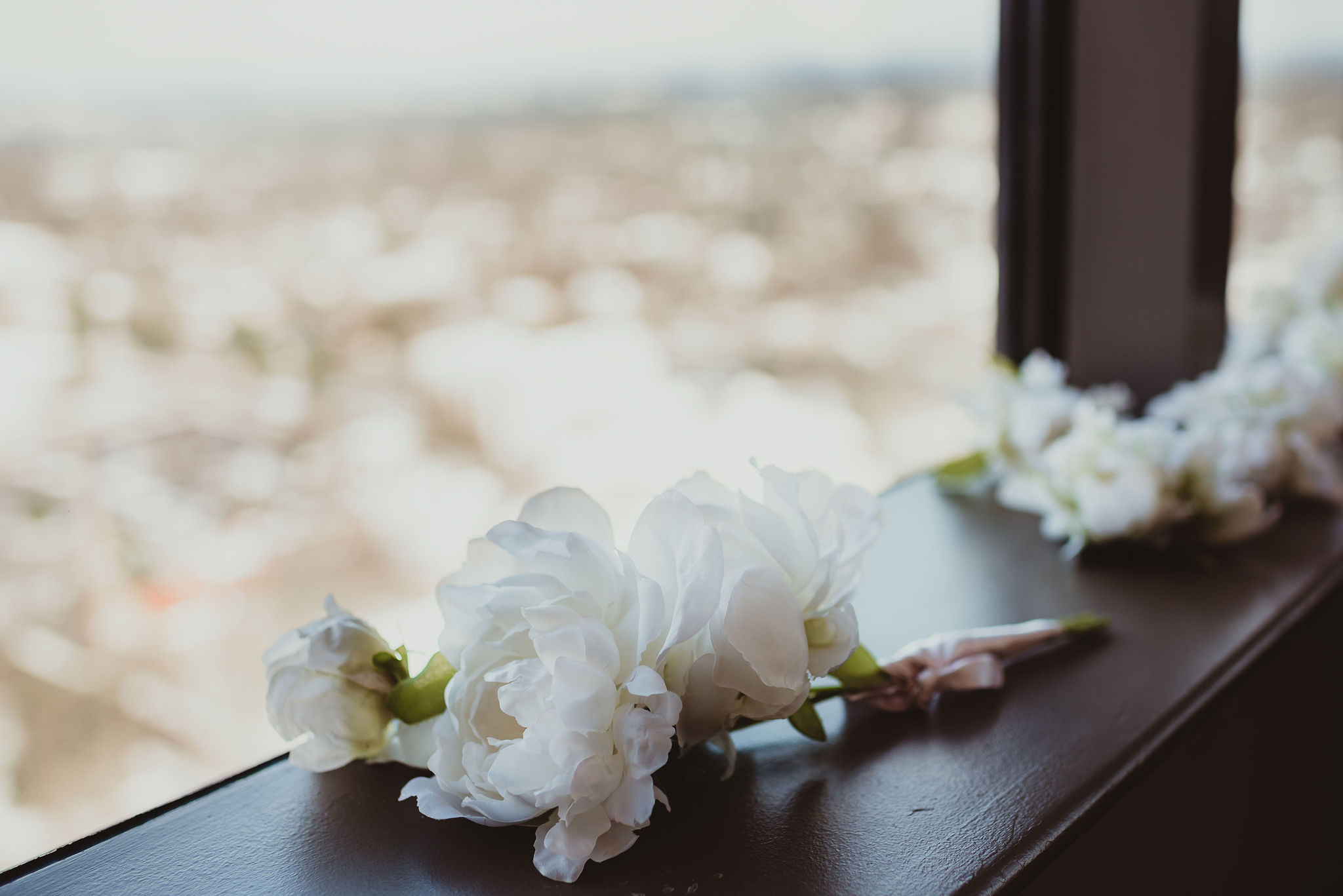 White floral boutonnieres sit on a windowsill. 