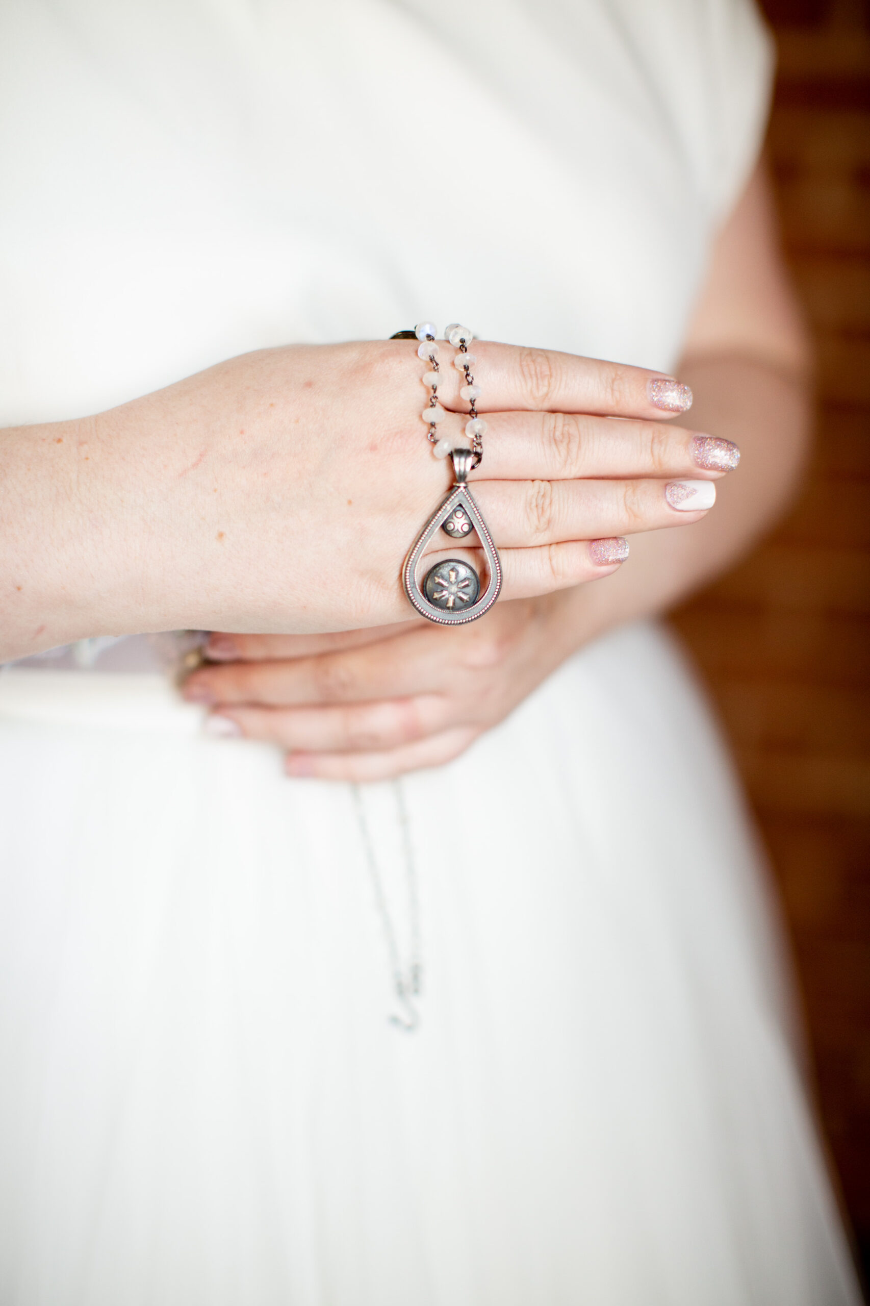 Close up on a pair of white hands holding a silver necklace against a wedding dress.