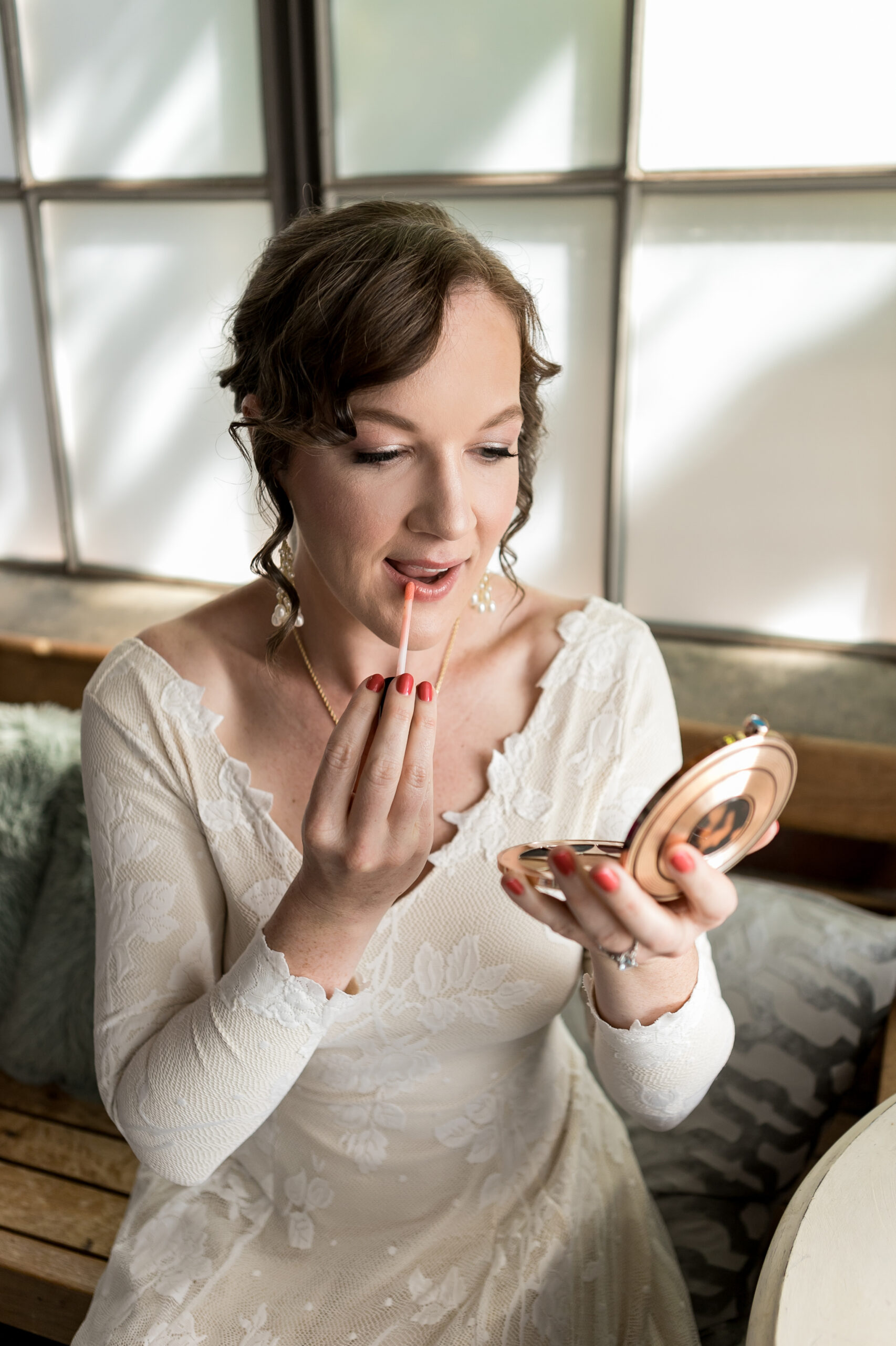 a bride in white applies lip gloss with a compact mirror.