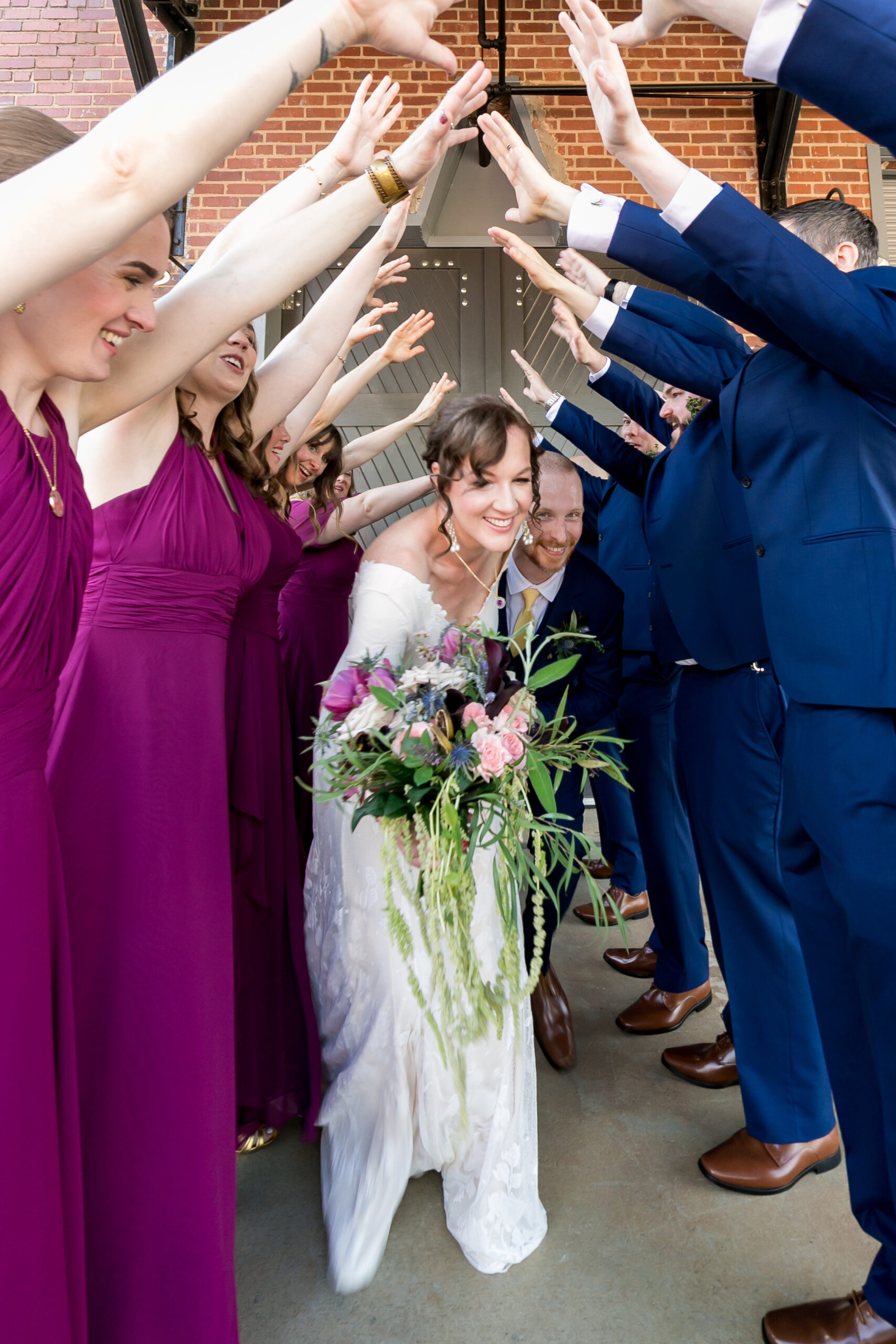 A wedding party forms a tunnel with their arms, through which a bride and groom run through. 