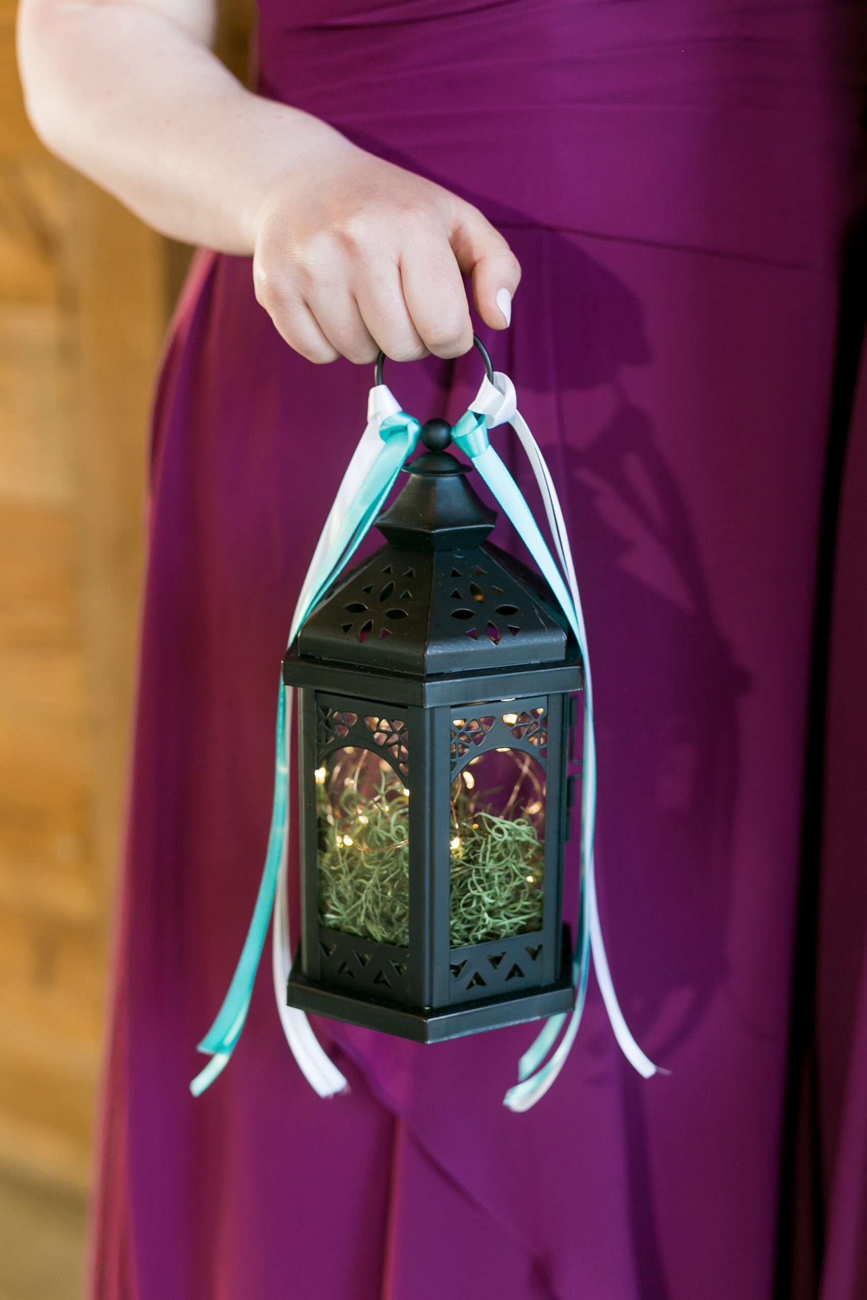 close up of a hand holding a black metal lantern. The lantern seems to contain moss and fairy lights.