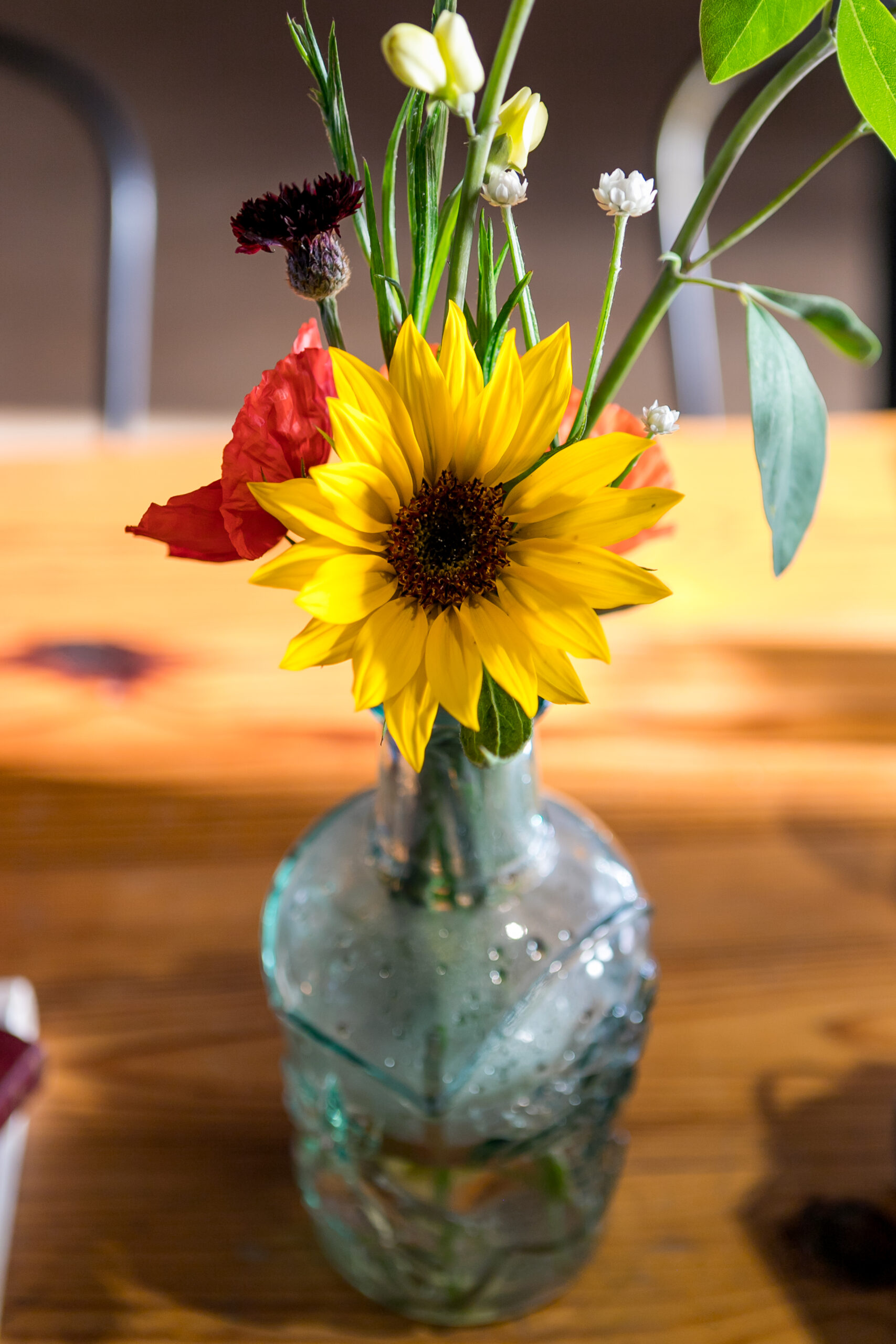 closeup on a bud vase with colorful blooms, including a sunflower.